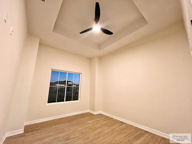 spare room with wood finished floors, a raised ceiling, a ceiling fan, and baseboards