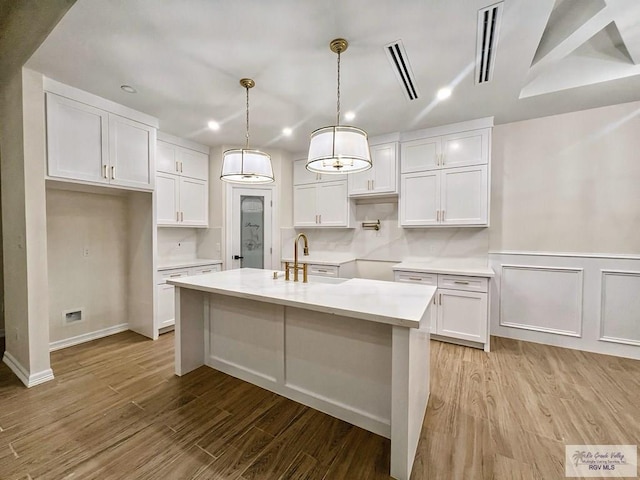 kitchen featuring a center island with sink, light countertops, light wood-style floors, white cabinets, and a sink