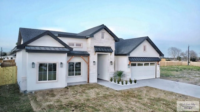 modern farmhouse with metal roof, fence, concrete driveway, stone siding, and a standing seam roof