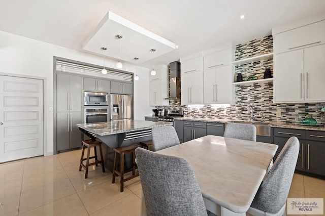 kitchen featuring pendant lighting, gray cabinets, appliances with stainless steel finishes, a kitchen island, and wall chimney range hood