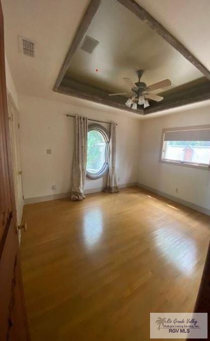 spare room with a tray ceiling, ceiling fan, and light hardwood / wood-style floors