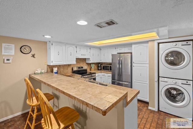 116 E Polaris Dr Unit 305, South Padre Island, TX 78597 - kitchen with stainless steel appliances, estacked washer and dryer, under cabinet range hood, a peninsula, and a kitchen breakfast bar