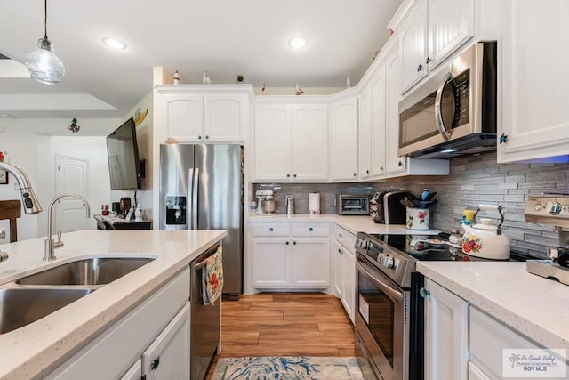 kitchen with appliances with stainless steel finishes, light wood-type flooring, sink, pendant lighting, and white cabinetry