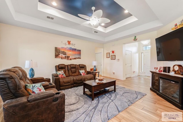 living room featuring a tray ceiling, ceiling fan, and light hardwood / wood-style floors