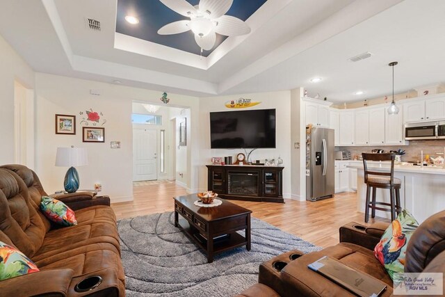 living room featuring a tray ceiling, ceiling fan, and light hardwood / wood-style flooring