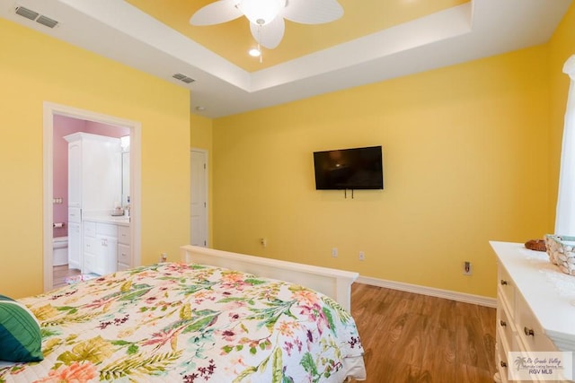 bedroom featuring ceiling fan, a raised ceiling, connected bathroom, and light hardwood / wood-style flooring