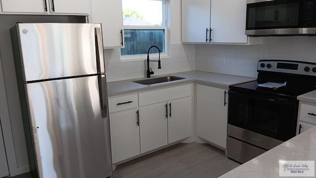 kitchen with light wood-type flooring, tasteful backsplash, stainless steel appliances, sink, and white cabinetry