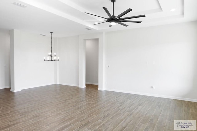 spare room with a raised ceiling, ceiling fan with notable chandelier, and light hardwood / wood-style flooring