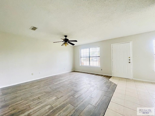 unfurnished room with ceiling fan, a textured ceiling, and light wood-type flooring