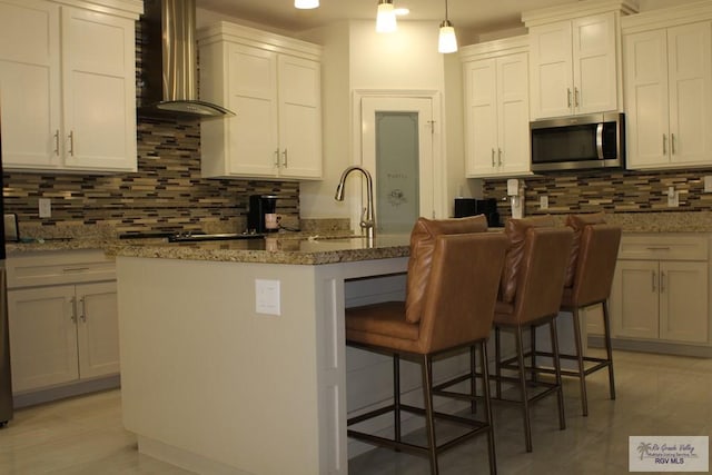 kitchen featuring a sink, a kitchen breakfast bar, stainless steel microwave, wall chimney range hood, and tasteful backsplash
