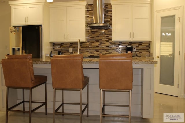 kitchen with wall chimney range hood, white cabinets, tasteful backsplash, and stainless steel refrigerator with ice dispenser