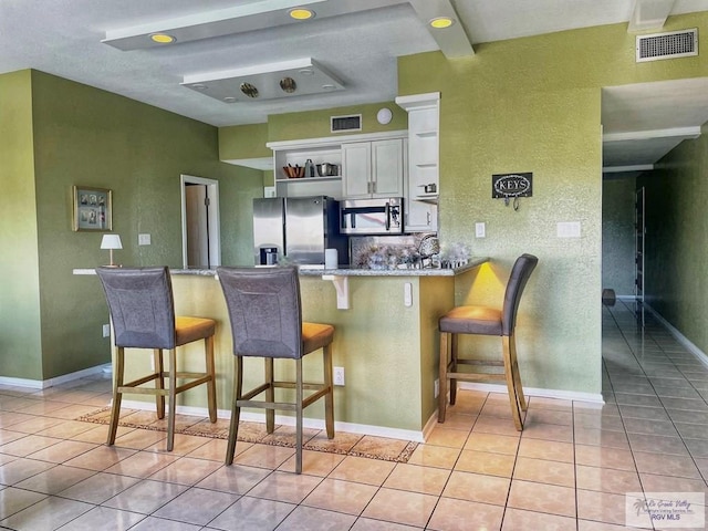 kitchen with white cabinets, appliances with stainless steel finishes, light tile patterned flooring, a kitchen bar, and kitchen peninsula