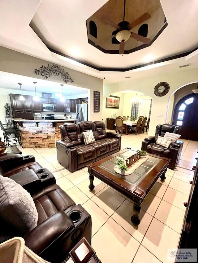 living room featuring arched walkways, a raised ceiling, light tile patterned flooring, and a ceiling fan