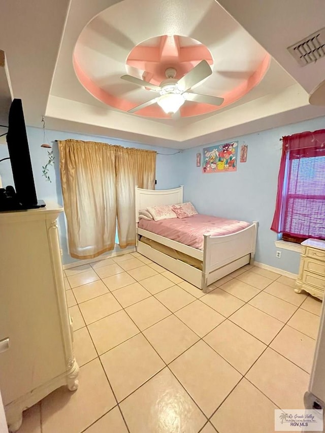 bedroom featuring a raised ceiling, light tile patterned flooring, and a ceiling fan