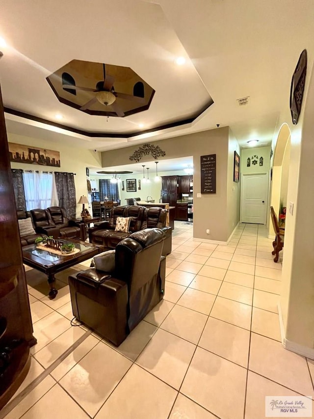 living room featuring a tray ceiling, a ceiling fan, arched walkways, and light tile patterned flooring