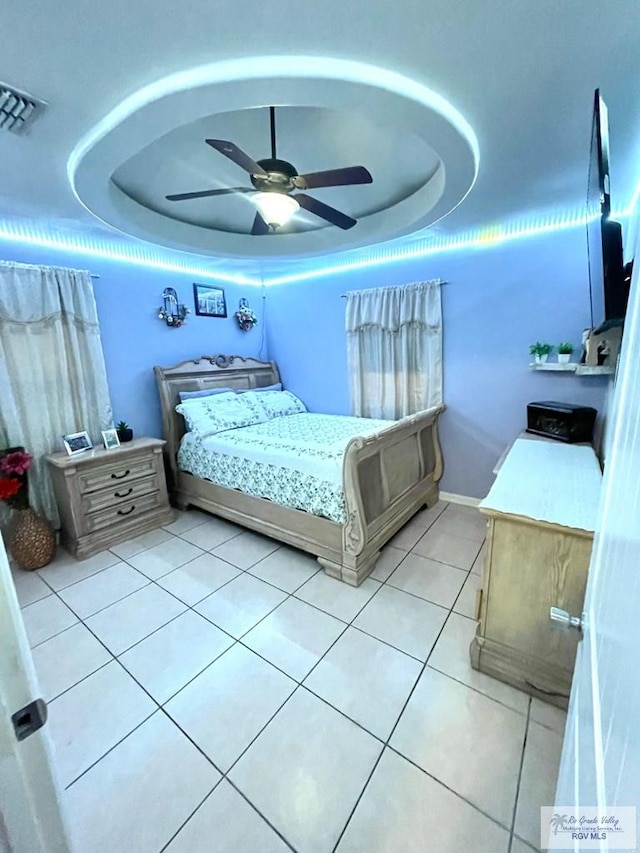 bedroom with a tray ceiling, light tile patterned flooring, and ceiling fan