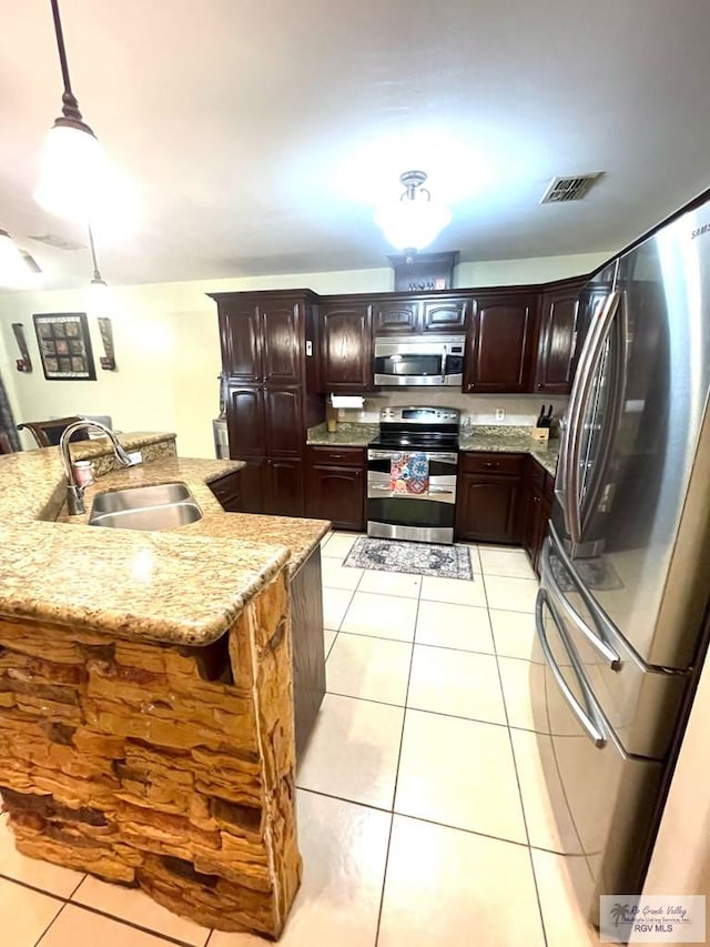 kitchen with stainless steel appliances, a sink, light tile patterned floors, light stone countertops, and dark brown cabinetry