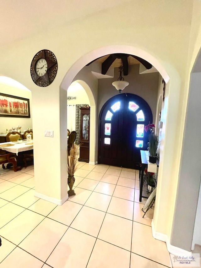foyer with light tile patterned flooring, arched walkways, and baseboards