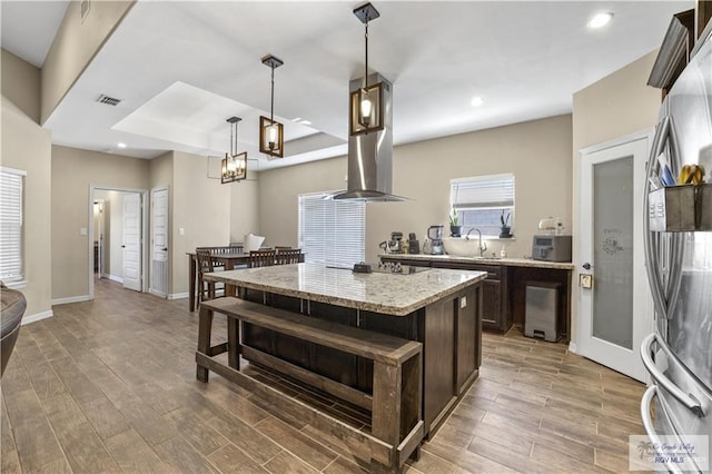 kitchen featuring pendant lighting, a kitchen island, sink, dark brown cabinets, and light stone counters