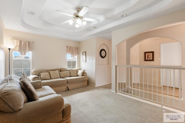 carpeted living area featuring baseboards, a raised ceiling, and ceiling fan