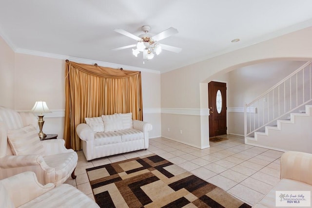 living area with stairs, ornamental molding, light tile patterned floors, arched walkways, and a ceiling fan