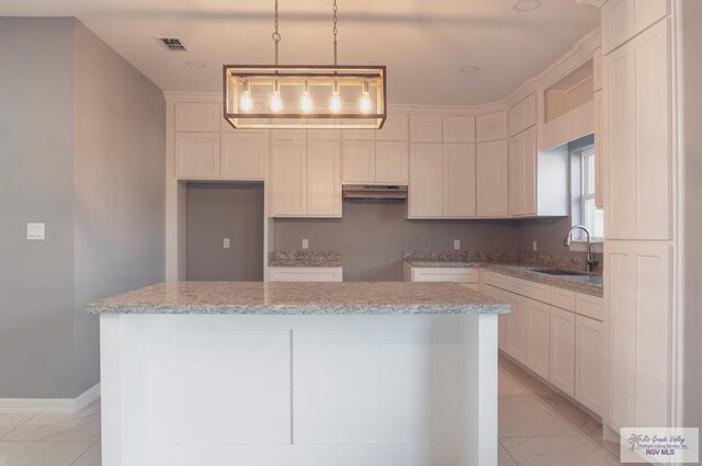 kitchen with white cabinets, decorative light fixtures, a kitchen island, and sink