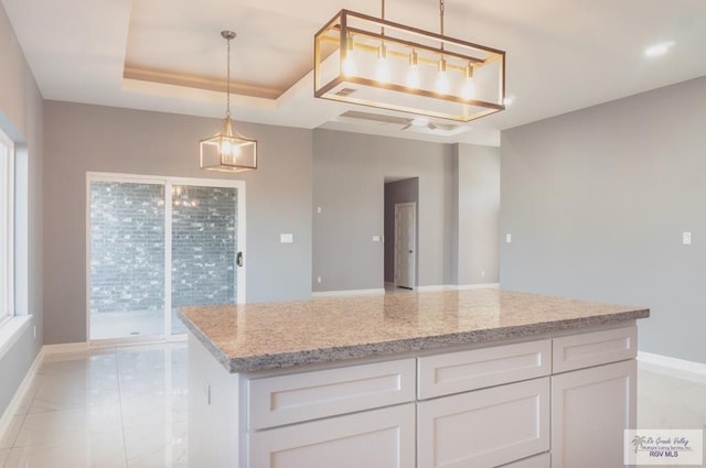 kitchen featuring light stone counters, a raised ceiling, white cabinets, a center island, and hanging light fixtures