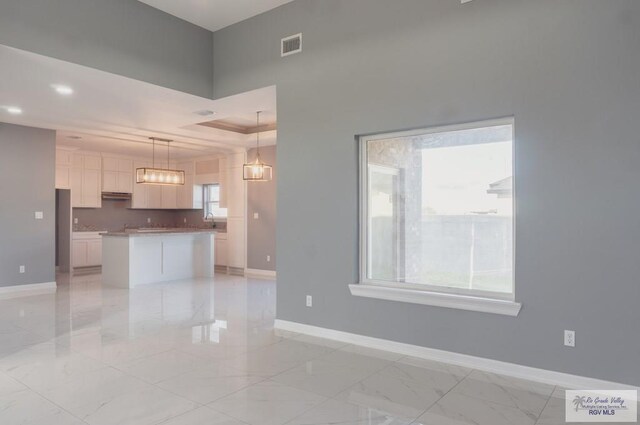 kitchen with a center island, white cabinets, a raised ceiling, sink, and hanging light fixtures