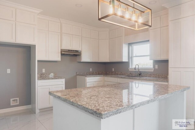 kitchen featuring white cabinetry, sink, a center island, light stone counters, and pendant lighting