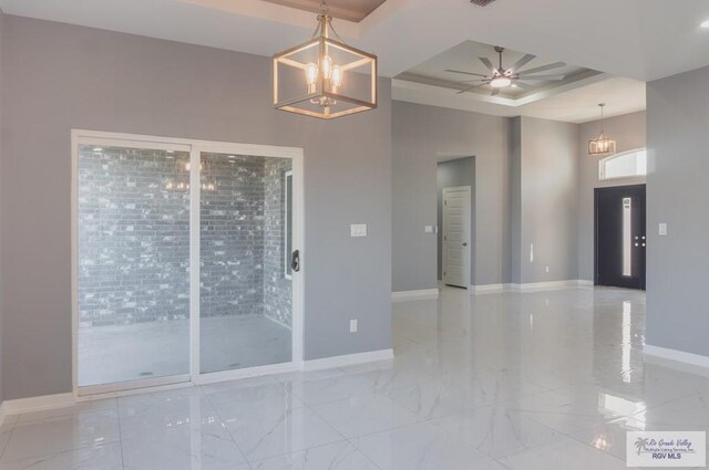 empty room with ceiling fan with notable chandelier and a raised ceiling