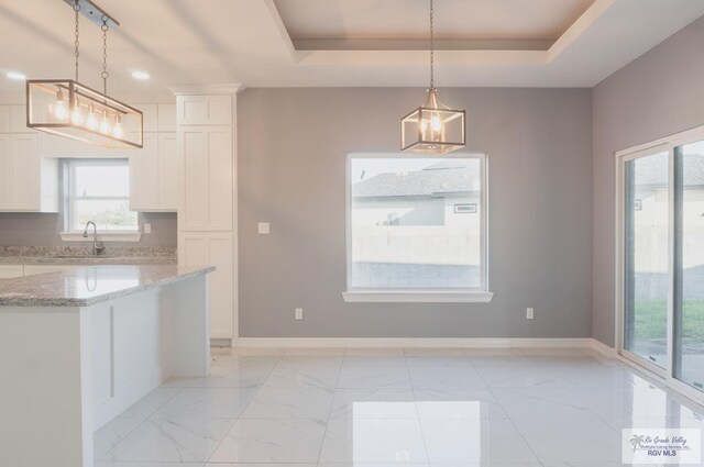 kitchen with white cabinetry, hanging light fixtures, and a tray ceiling