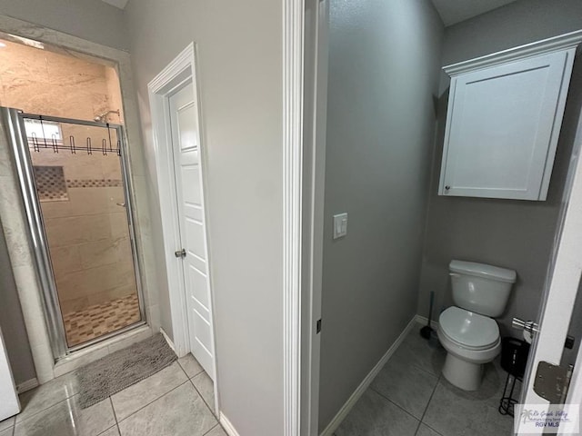 bathroom with toilet, tile patterned floors, a shower stall, and baseboards