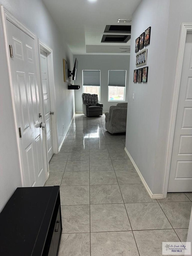 corridor with baseboards, a raised ceiling, and light tile patterned flooring