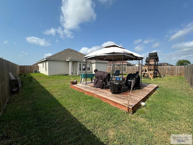 rear view of property featuring a lawn, a deck, a gazebo, a fenced backyard, and a playground