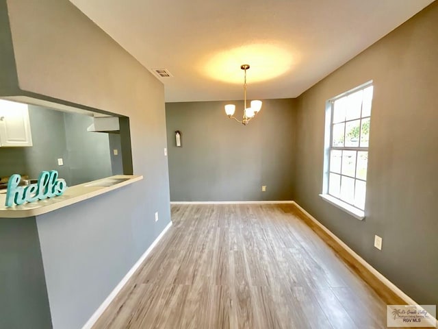 unfurnished dining area with a chandelier, wood finished floors, visible vents, and baseboards