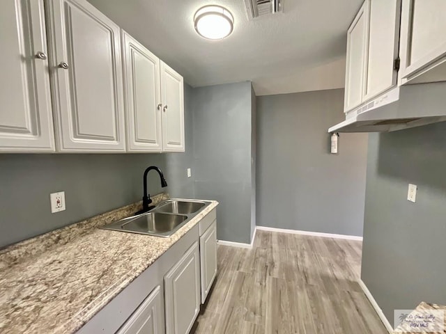 kitchen featuring light wood finished floors, a sink, baseboards, visible vents, and white cabinetry
