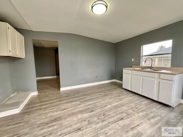 kitchen with a sink, light wood-style flooring, baseboards, white cabinets, and lofted ceiling