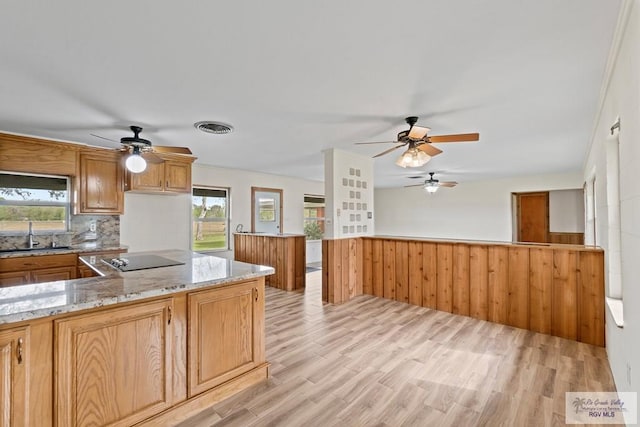 kitchen with sink, tasteful backsplash, light hardwood / wood-style floors, wooden walls, and black electric stovetop