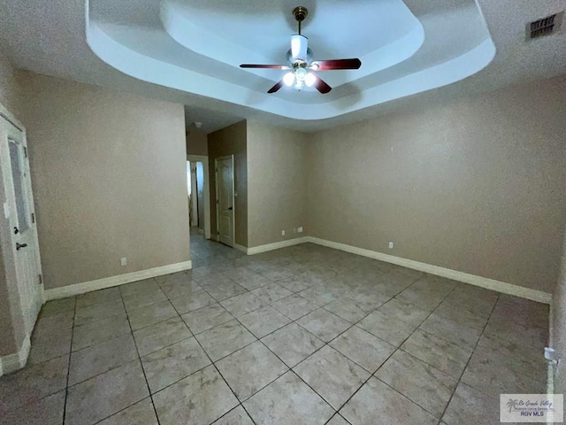 tiled spare room featuring a tray ceiling and ceiling fan