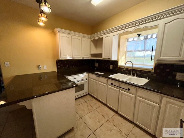 kitchen with kitchen peninsula, sink, decorative light fixtures, white cabinets, and oven