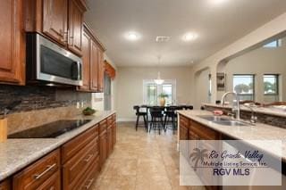 kitchen featuring sink, decorative backsplash, light stone countertops, black electric cooktop, and decorative light fixtures