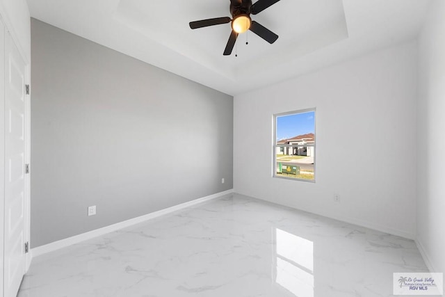 empty room featuring ceiling fan and a raised ceiling