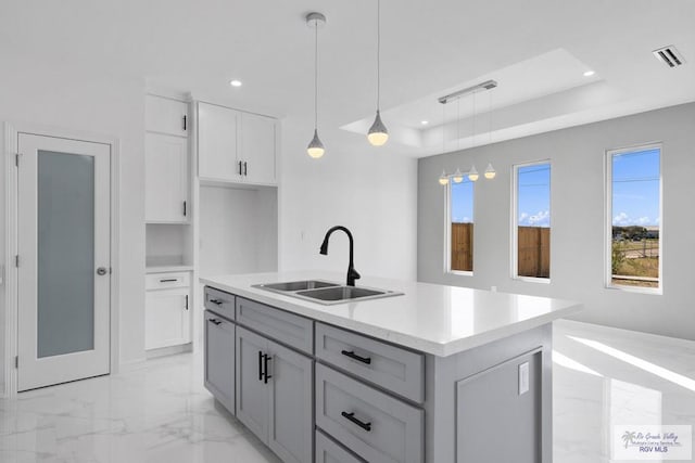 kitchen with a kitchen island with sink, white cabinets, sink, gray cabinets, and decorative light fixtures