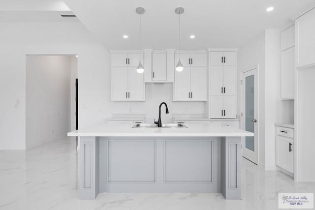 kitchen with a center island with sink, white cabinets, hanging light fixtures, and sink