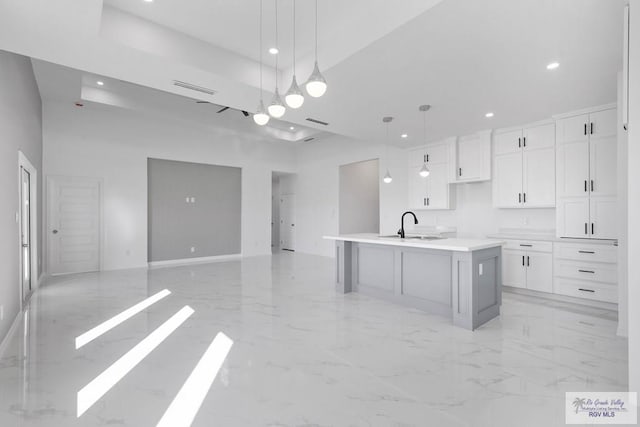 kitchen featuring white cabinets, sink, an island with sink, and hanging light fixtures