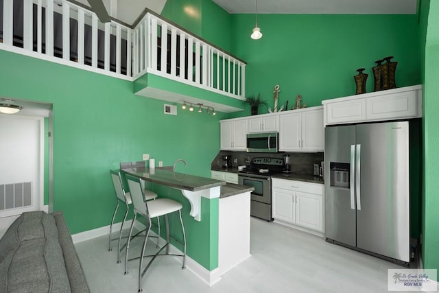 kitchen featuring a kitchen bar, stainless steel appliances, white cabinets, hanging light fixtures, and a high ceiling