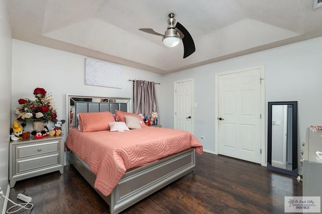 bedroom featuring a tray ceiling, dark wood finished floors, baseboards, and ceiling fan