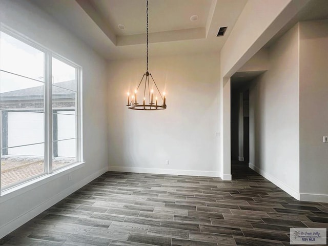 unfurnished dining area with a tray ceiling, a notable chandelier, dark wood finished floors, visible vents, and baseboards