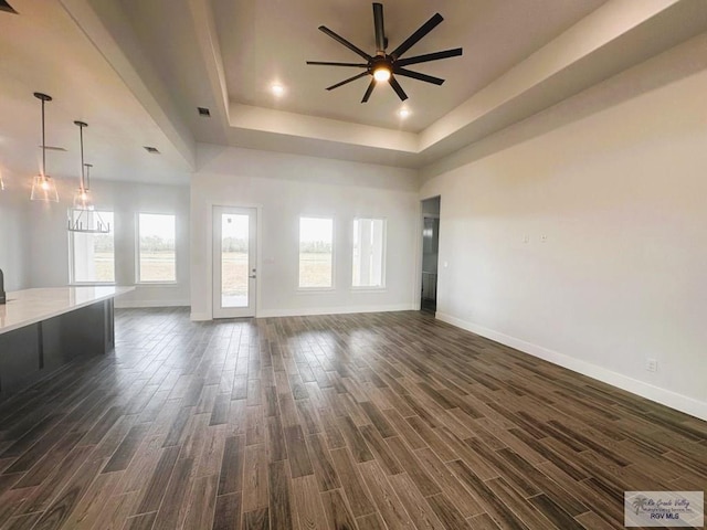 unfurnished living room featuring dark wood-style floors, a tray ceiling, ceiling fan, and baseboards