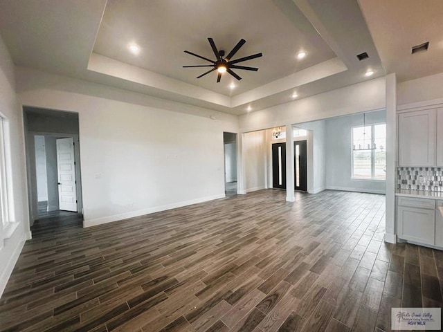 unfurnished living room featuring a tray ceiling, dark hardwood / wood-style flooring, and ceiling fan with notable chandelier